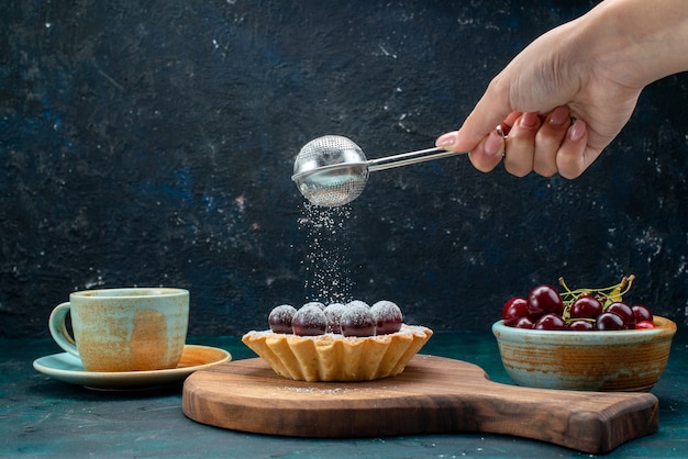 Cupcake mit Kirschen neben Latte und Frau, die Zuckerpulver sieben