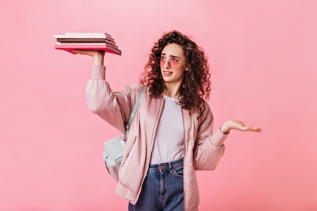 Curly Frau betrachtet Bücher und posiert auf rosa Hintergrund