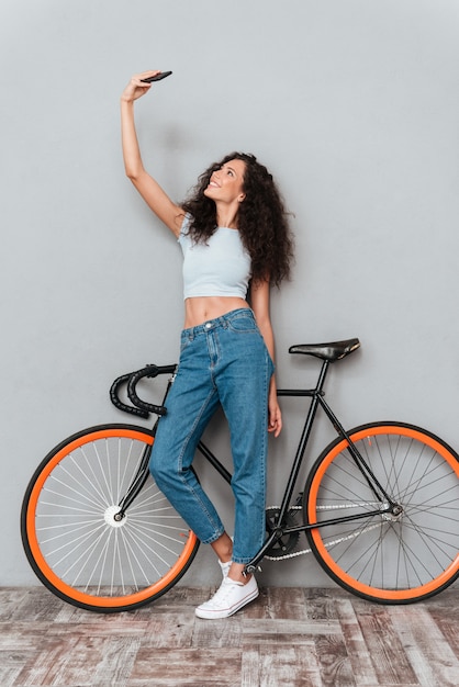 Curly Frau macht Selfie auf Smartphone mit Fahrrad