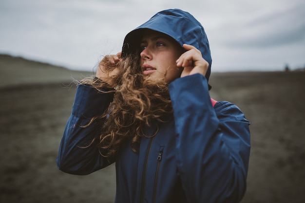 Curly Model steht am Strand und genießt den kalten Herbsttag mit einer Kapuze auf dem Kopf