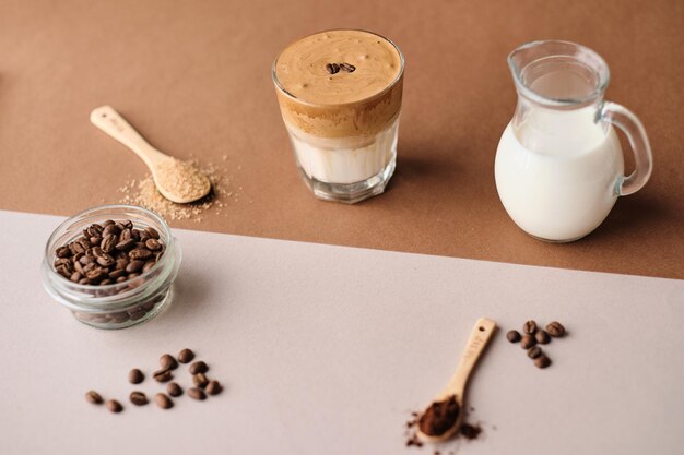 Dalgona-Eiskaffee mit Mandelmilch und braunen Zuckerkaffeebohnen auf einem beigen Blatt Ein Glas trendige, flauschige Koreith-Schlagsahne