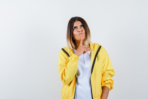 Dame, die Finger auf Kinn im T-Shirt, in der Jacke hält und hoffnungsvoll aussieht, Vorderansicht.