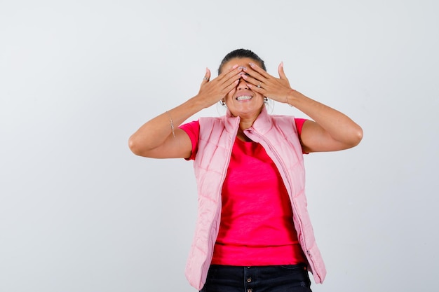 Dame hält die Hände auf den Augen in T-Shirt, Weste und sieht glücklich aus