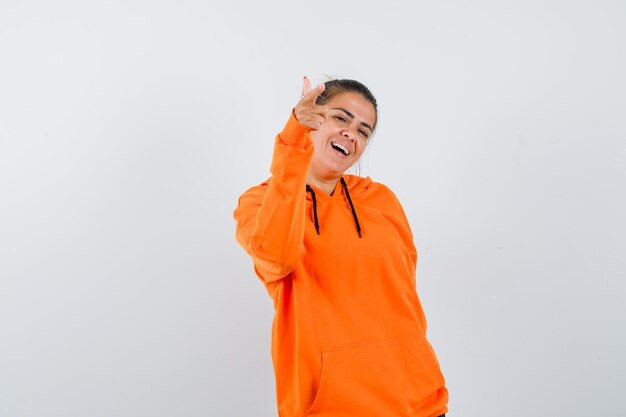 Dame im orangefarbenen Hoodie, der auf die Kamera zeigt und fröhlich aussieht