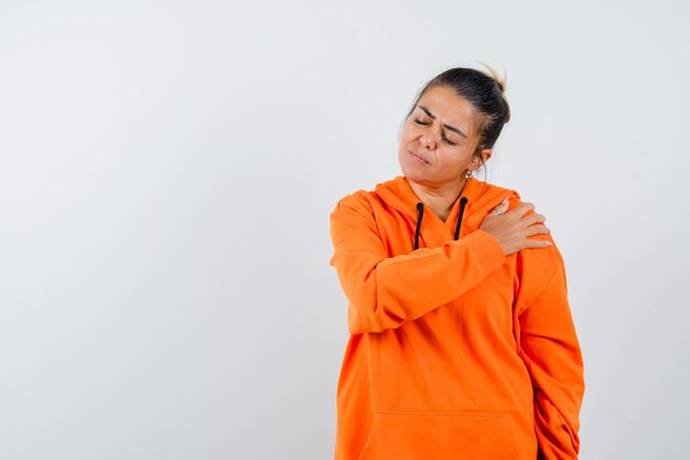 Dame im orangefarbenen Hoodie, die Hand auf ihrer Schulter hält und friedlich aussieht looking