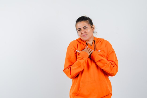 Dame im orangefarbenen Hoodie hält die Hände auf der Brust und sieht fröhlich aus