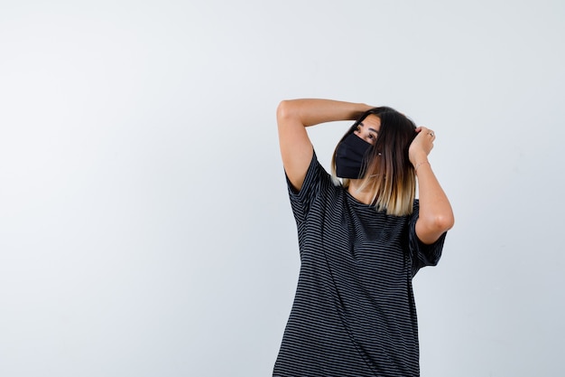 Dame im schwarzen Kleid, medizinische Maske, die Hände auf Kopf hält und nachdenklich schaut, Vorderansicht.