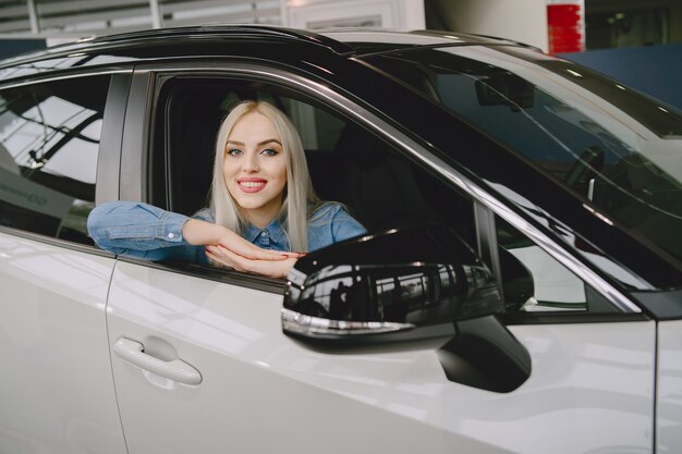 Dame in einem Autosalon. Frau, die das Auto kauft. Elegante Frau in einem blauen Kleid.