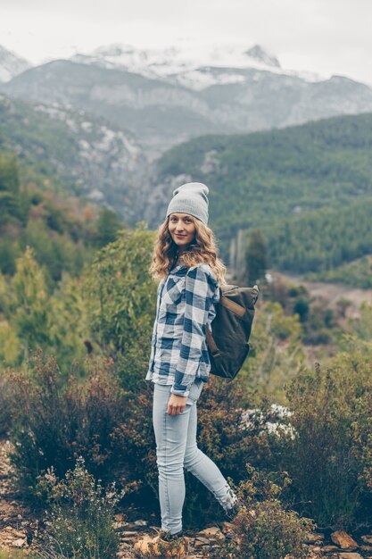 Dame in grauem Hut und Jeans, die tagsüber in der Natur stehen und lächeln