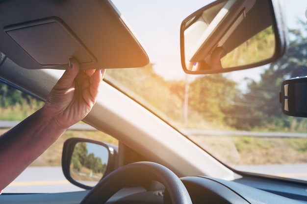 Dame justieren Sonnenblende beim Fahren des Autos auf Landstraßenstraße - Innenauto unter Verwendung des Konzeptes