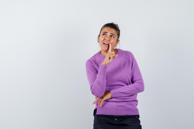 Dame steht in denkender Pose in Wollbluse und schaut zögernd