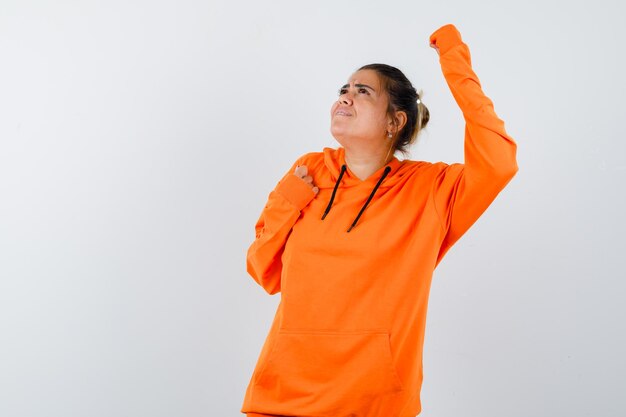 Dame zeigt Gewinnergeste in orangefarbenem Hoodie und sieht glücklich aus looking