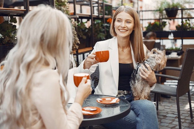 Damen trinken einen Kaffee. Frauen sitzen am Tisch. Freunde mit einem niedlichen Hund.