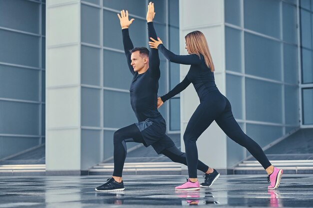 Das athletische Fitness-Paar dehnt sich über den modernen Gebäudehintergrund aus. Ganzkörperbild.