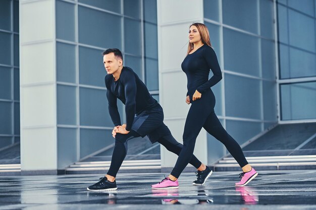 Das athletische Fitness-Paar dehnt sich über den modernen Gebäudehintergrund aus. Ganzkörperbild.