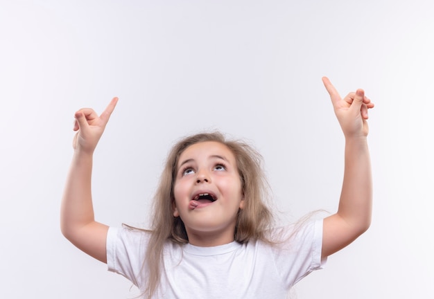 Das Aufschauen des kleinen Schulmädchens, das weißes T-Shirt trägt, zeigt auf lokalisierten weißen Hintergrund