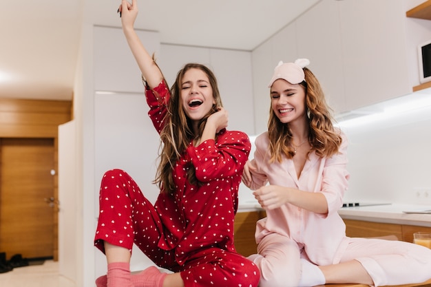 Das begeisterte Mädchen trägt rosa Socken und einen hellen Pyjama, der vor Vergnügen posiert. Innenporträt der prächtigen jungen Damen, die Morgen zu Hause verbringen.