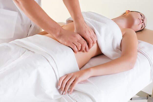 Das Bild der schönen Frau im Massagesalon und in den männlichen Händen auf ihrem Körper