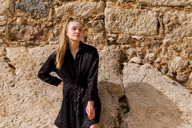 Das blonde Mädchen schaut links im schwarzen Kleid auf Steinhintergrund