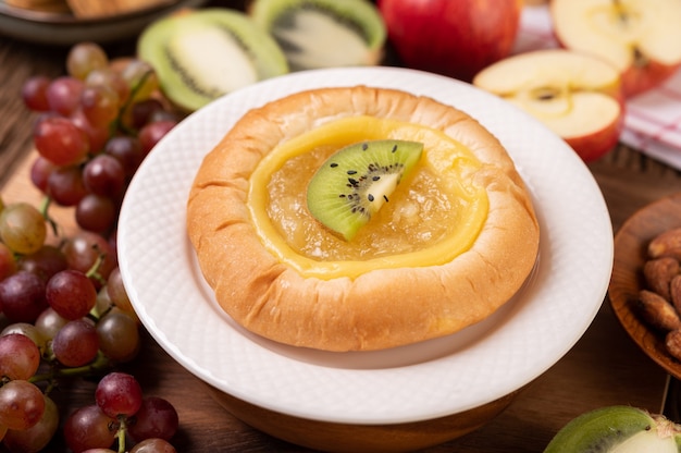 Das Brot mit Marmelade bestreichen und mit Kiwi und Trauben den Apfel auf den Holztisch legen