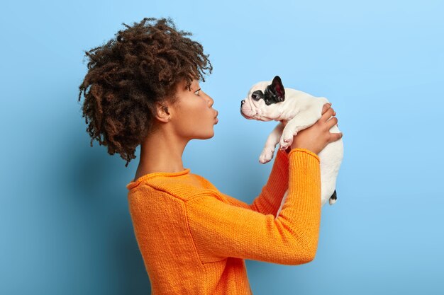 Das erwachsene Afro-Mädchen steht im Profil und zieht einen kleinen Welpen in die Luft