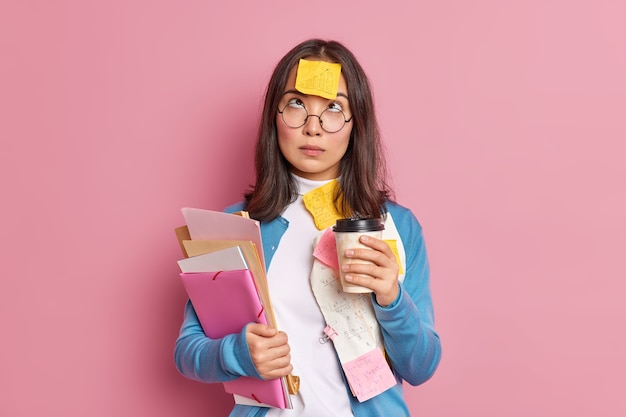 Kostenloses Foto das foto einer ernsthaften studentin hat eine kaffeepause, die oben konzentriert ist und einen erinnerungsaufkleber auf der stirn hat