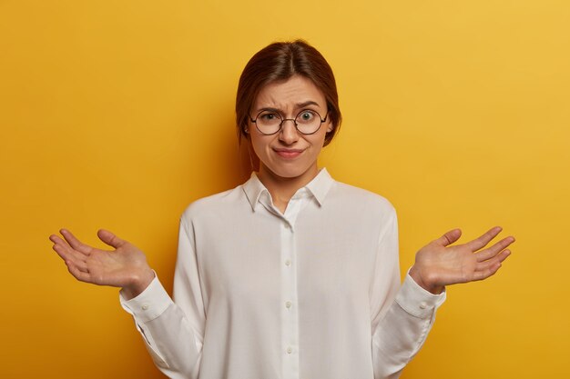 Das Foto einer unzufriedenen zögernden Frau spreizt die Handflächen, runzelt die Stirn und sieht genervt aus. Sie kann keinen Ausweg aus einem schwierigen Rätsel erkennen