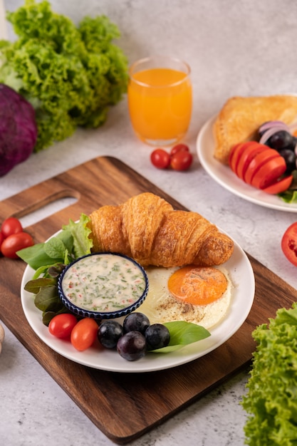 Das Frühstück besteht aus Croissant, Spiegelei, Salatdressing, schwarzen Trauben und Tomaten.