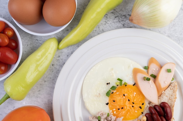 Das Frühstück besteht aus Spiegeleiern, Wurst, gehacktem Schweinefleisch, Brot, roten Bohnen und Soja auf einem weißen Teller.