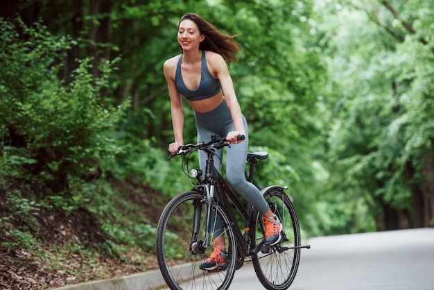 Das fühlt sich großartig an. Weiblicher Radfahrer auf einem Fahrrad auf Asphaltstraße im Wald am Tag