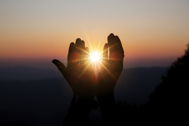 Das geistige Gebet überreicht Sonnenschein mit unscharfem schönen Sonnenuntergang