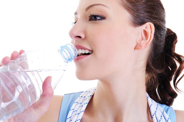 Das Gesicht der jungen Frau der Nahaufnahme mit einer Flasche Wasser nahe ihren Lippen