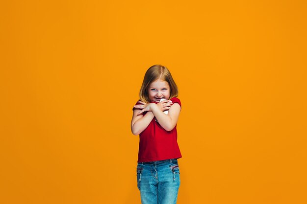Das glückliche jugendlich Mädchen, das gegen orange Hintergrund steht und lächelt.