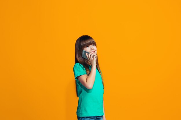 Das glückliche jugendlich Mädchen, das gegen orange Wand steht und lächelt