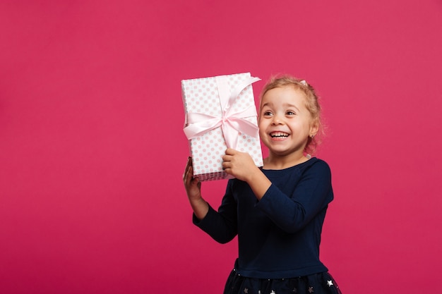 Das glückliche junge blonde Mädchen, das Geschenkbox hält und freut sich