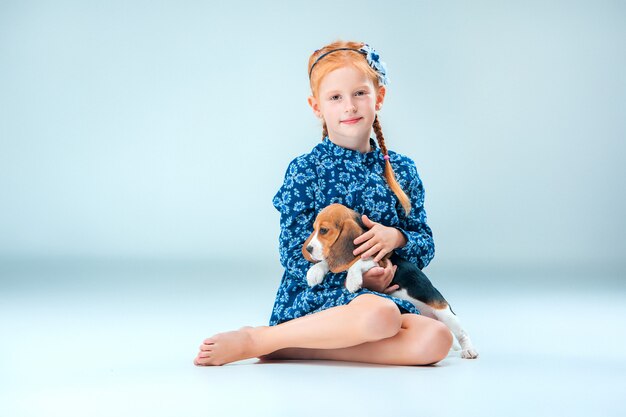 Das glückliche Mädchen und ein Beagle-Welpe auf grauer Wand