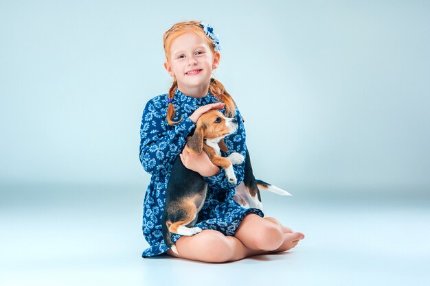 Das glückliche Mädchen und ein Beagle-Welpe auf grauer Wand