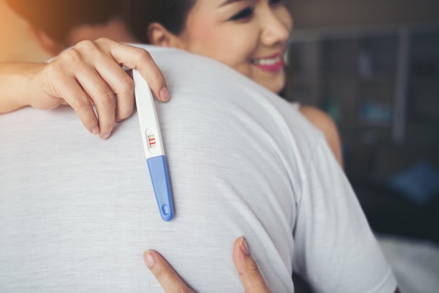 Das glückliche Paar, das nach lächelt, finden positiven Schwangerschaftstest im Schlafzimmer heraus