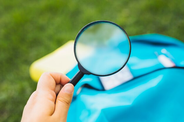 Das Halten des Vergrößerungsglases erhöht den Hintergrund des Rucksacks auf Gras