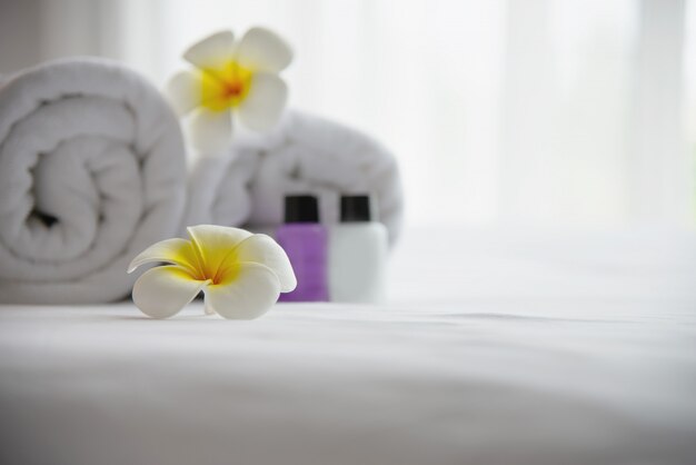 Das Hoteltuch und die Shampoo- und Seifenbadflasche, die auf weißes Bett mit der Plumeriablume verziert wurden - entspannen Sie sich Ferien am Hotelerholungsortkonzept