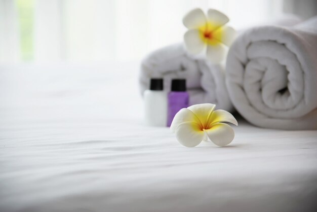 Das Hoteltuch und die Shampoo- und Seifenbadflasche, die auf weißes Bett mit der Plumeriablume verziert wurden - entspannen Sie sich Ferien am Hotelerholungsortkonzept