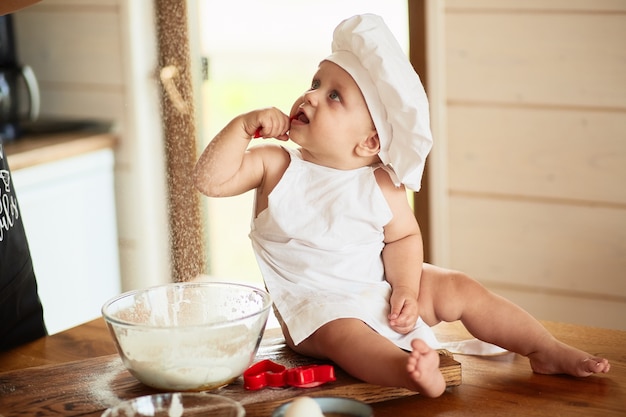 Das hübsche Baby sitzt nahe Platte mit Mehl