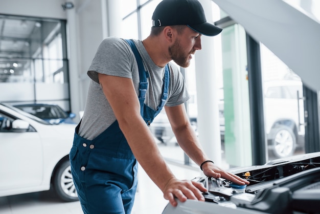 Das ist eine einfache Aufgabe für diesen Kerl. Mann in blauer Uniform und schwarzem Hut, der beschädigtes Automobil repariert