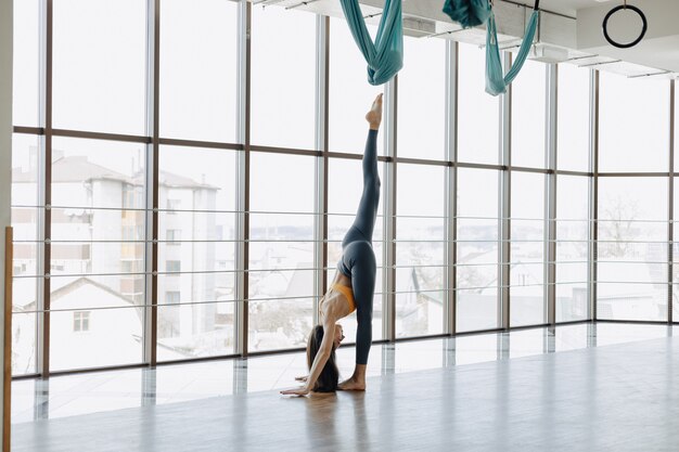 Das junge attraktive Mädchen, das Eignung tut, trainiert mit Yoga auf dem Boden gegen die Oberfläche von panoramischen Fenstern