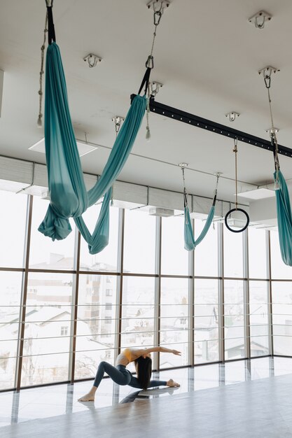 Das junge attraktive Mädchen, das Eignung tut, trainiert mit Yoga auf dem Boden vor dem hintergrund der panoramischen Fenster