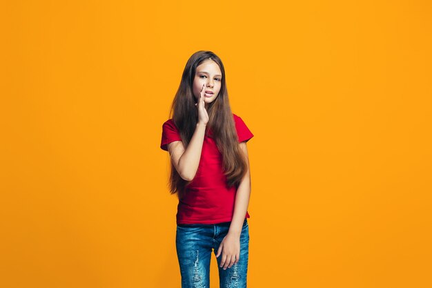 Das junge jugendlich Mädchen flüstert ein Geheimnis hinter ihrer Hand über orange Hintergrund