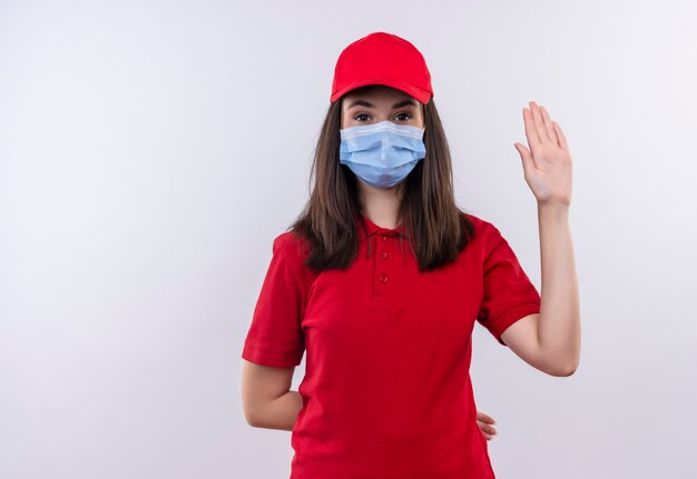 Das junge Liefermädchen, das rotes T-Shirt in der roten Kappe trägt, trägt eine Maske zeigt Stoppgeste auf lokalem weißem Hintergrund