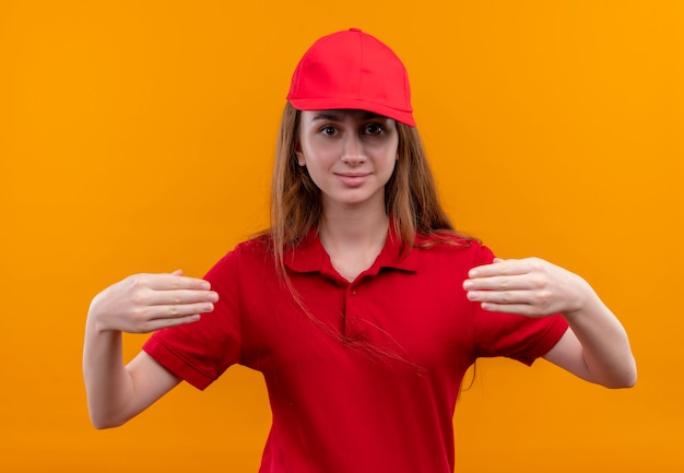 Das junge Liefermädchen in der roten Uniform gibt vor, etwas auf der isolierten orangefarbenen Wand zu halten