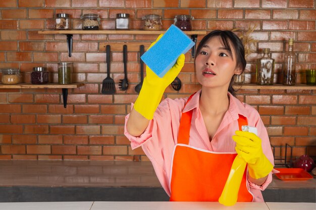 Das junge Mädchen trägt gelbe Handschuhe, während es den Küchenraum mit Staubtuch in ihrem Haus putzt.