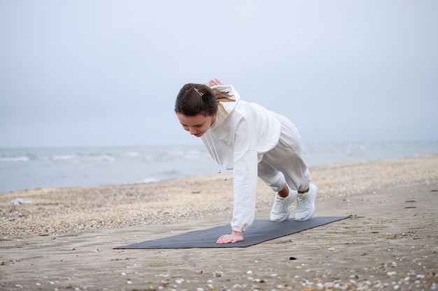 Kostenloses Foto das junge schöne mädchen, das auf der yogamatte liegt und einarmige liegestütze macht foto in hoher qualität